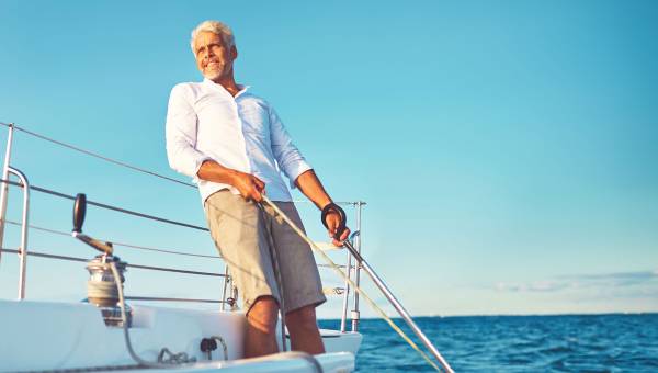 Ein Mann steht auf einem Segelschiff, schaut in die Ferne, lehnt sich zurück und hält kraftvoll ein Seil in Händen