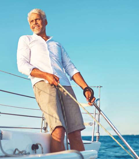 Ein Mann steht auf einem Segelschiff, schaut in die Ferne, lehnt sich zurück und hält kraftvoll ein Seil und die Steuerverlängerung fest